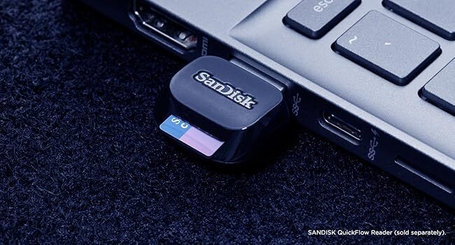 Close-up view of a SanDisk USB drive inserted into a laptop's USB port, photographed against a dark surface with partial keyboard visible.