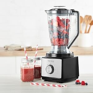 Modern countertop blender with stainless steel base and clear pitcher containing red smoothie. Wooden utensils and fresh berries visible in background.